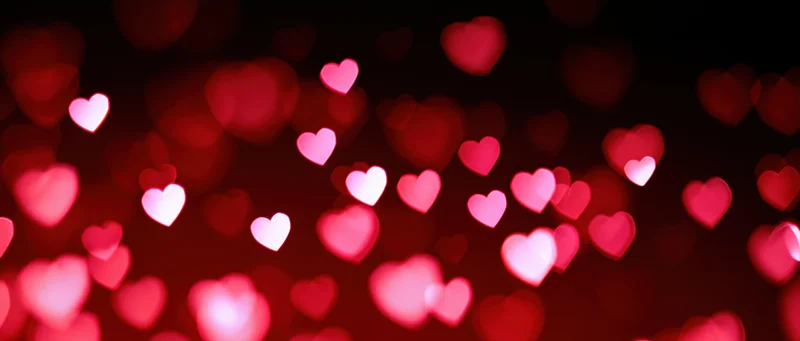 Scattered heart-shaped bokeh lights in red and pink against a dark background