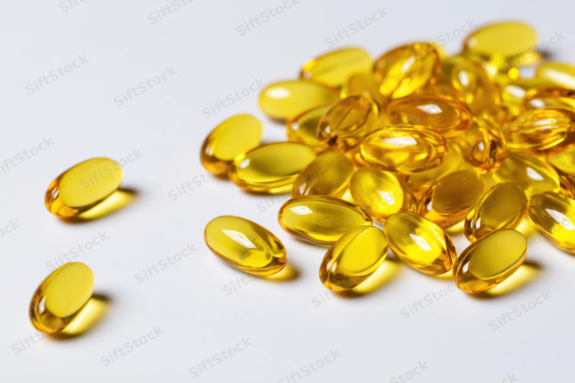 Scattered translucent yellow oval gel capsules of fish oil on white surface