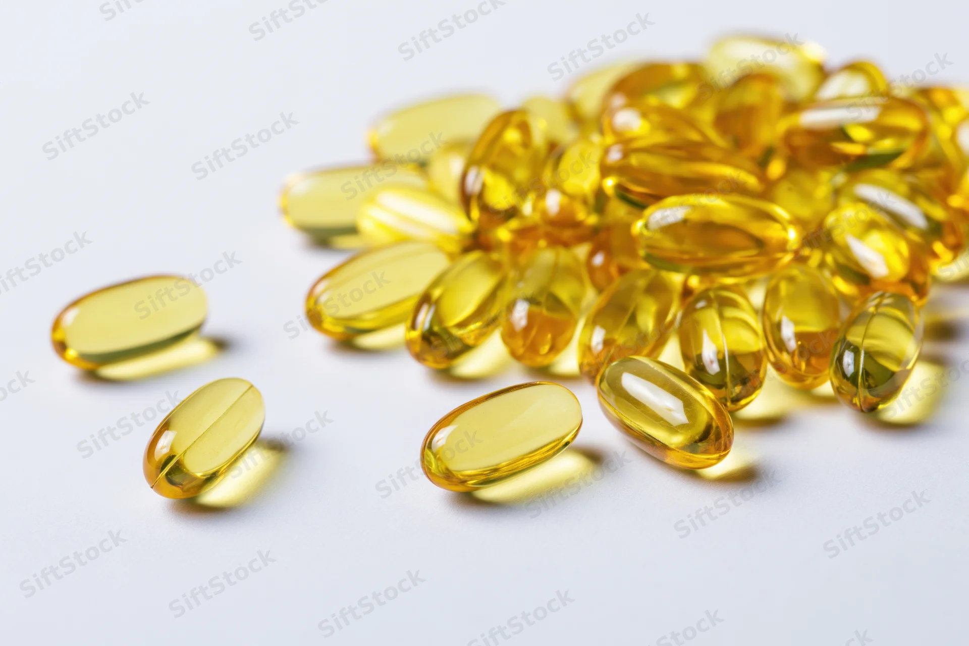 Scattered translucent yellow oval gel capsules of fish oil on white surface