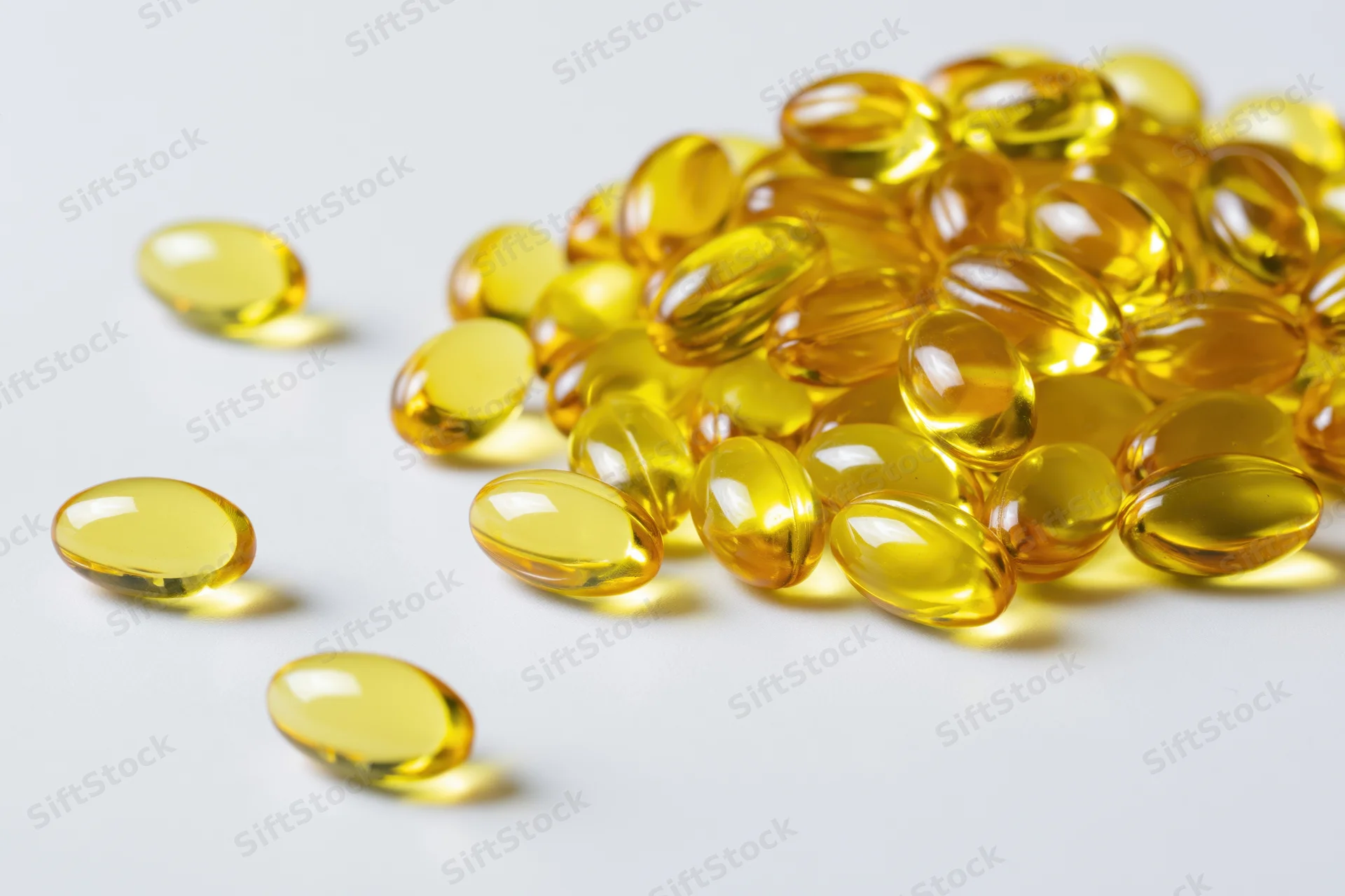 Scattered translucent yellow oval gel capsules of fish oil on white surface