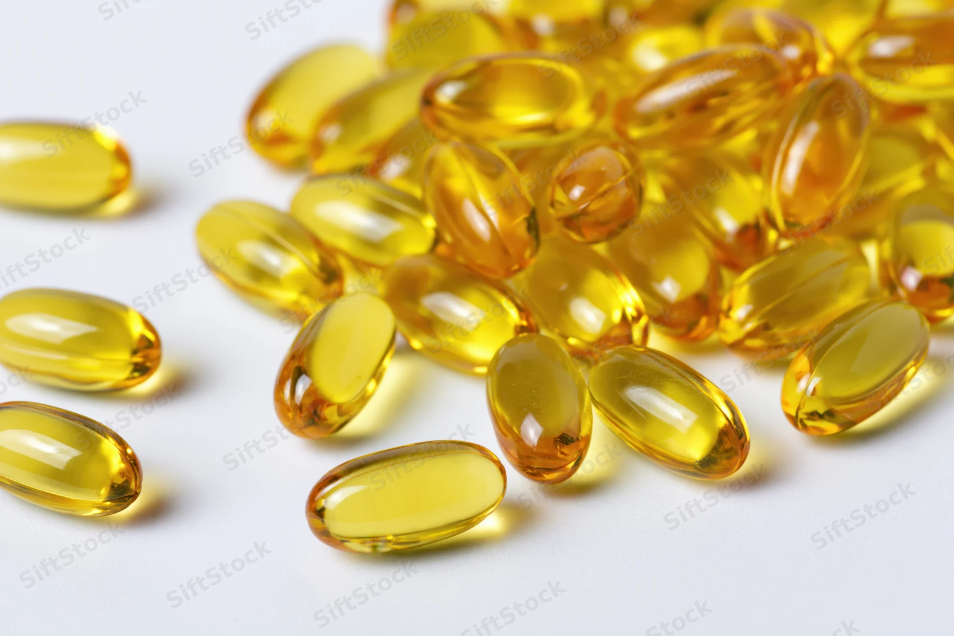 Scattered translucent yellow oval gel capsules of fish oil on white surface