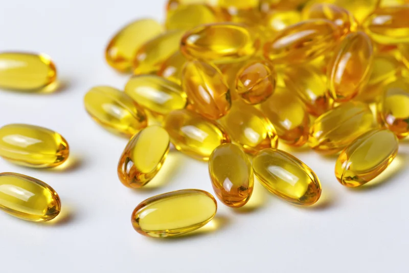Scattered translucent yellow oval gel capsules of fish oil on white surface