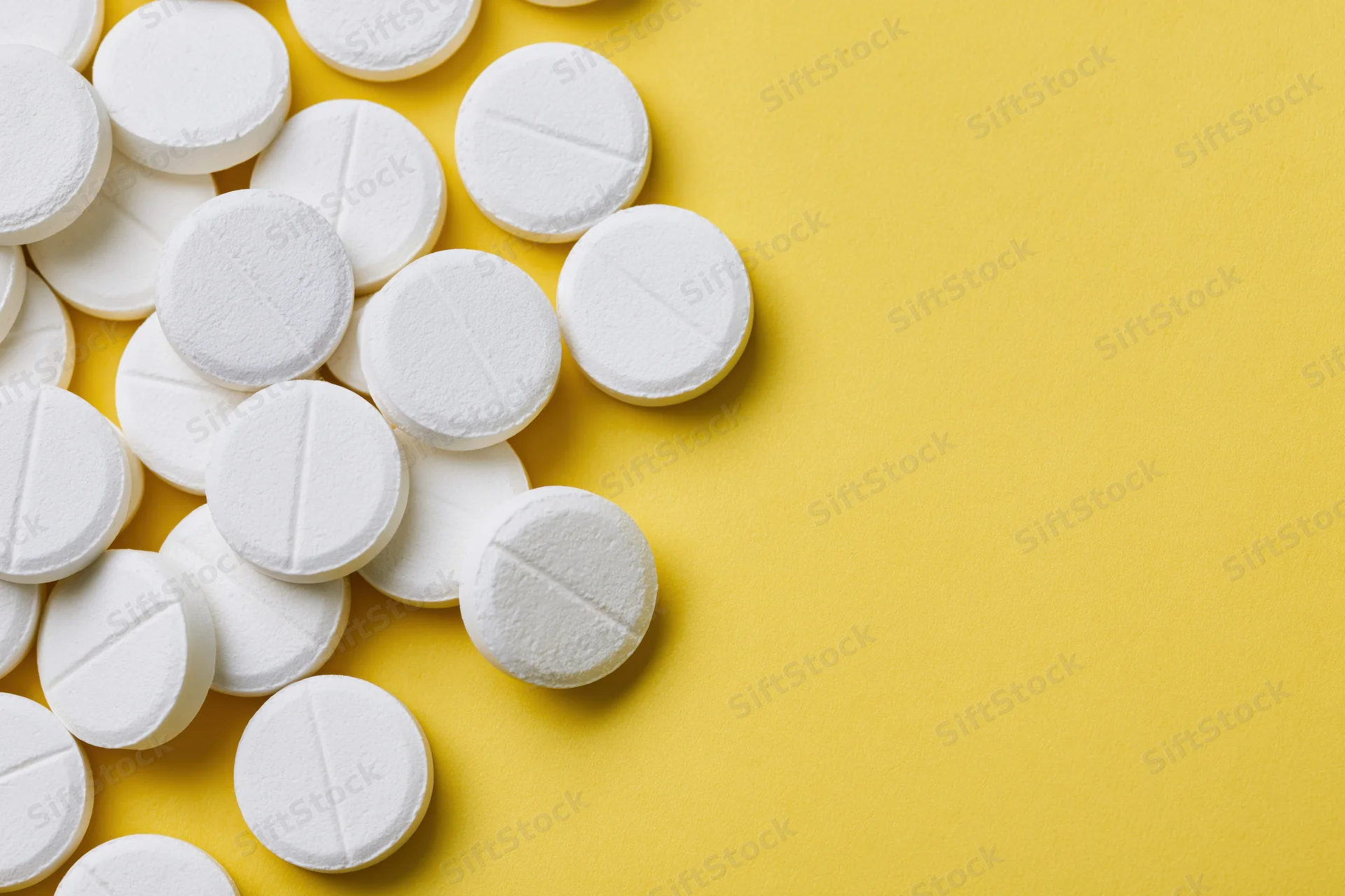 White pharmaceutical tablets scattered on yellow surface with copyspace