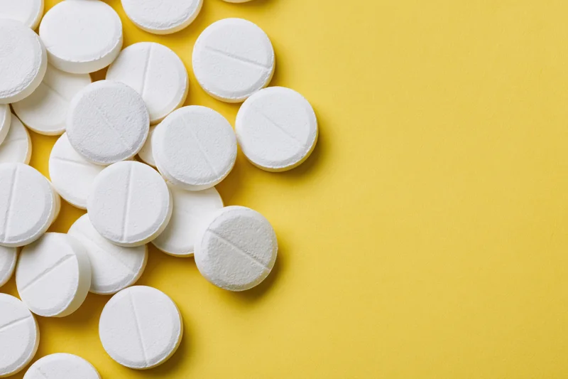 White pharmaceutical tablets scattered on yellow surface with copyspace