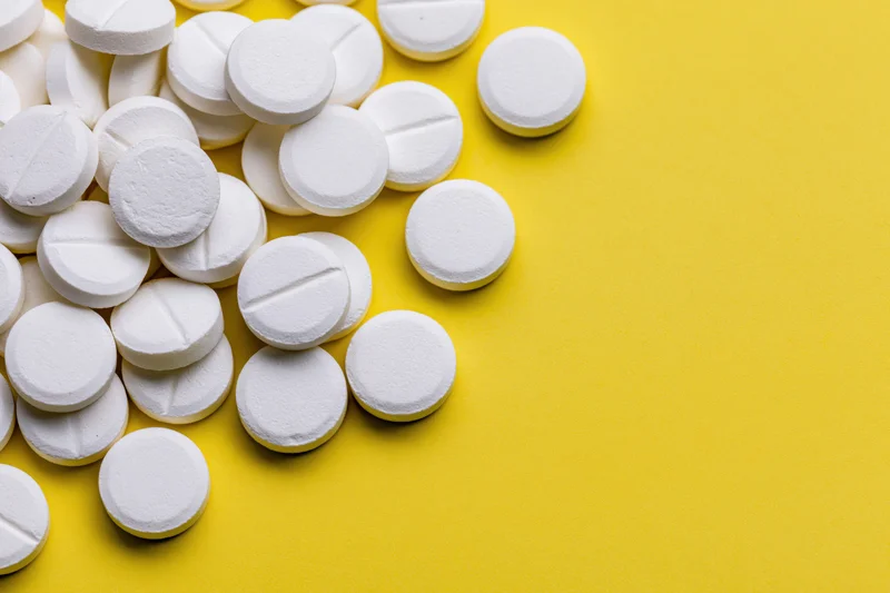 White round pharmaceutical tablets scattered on yellow surface with copyspace