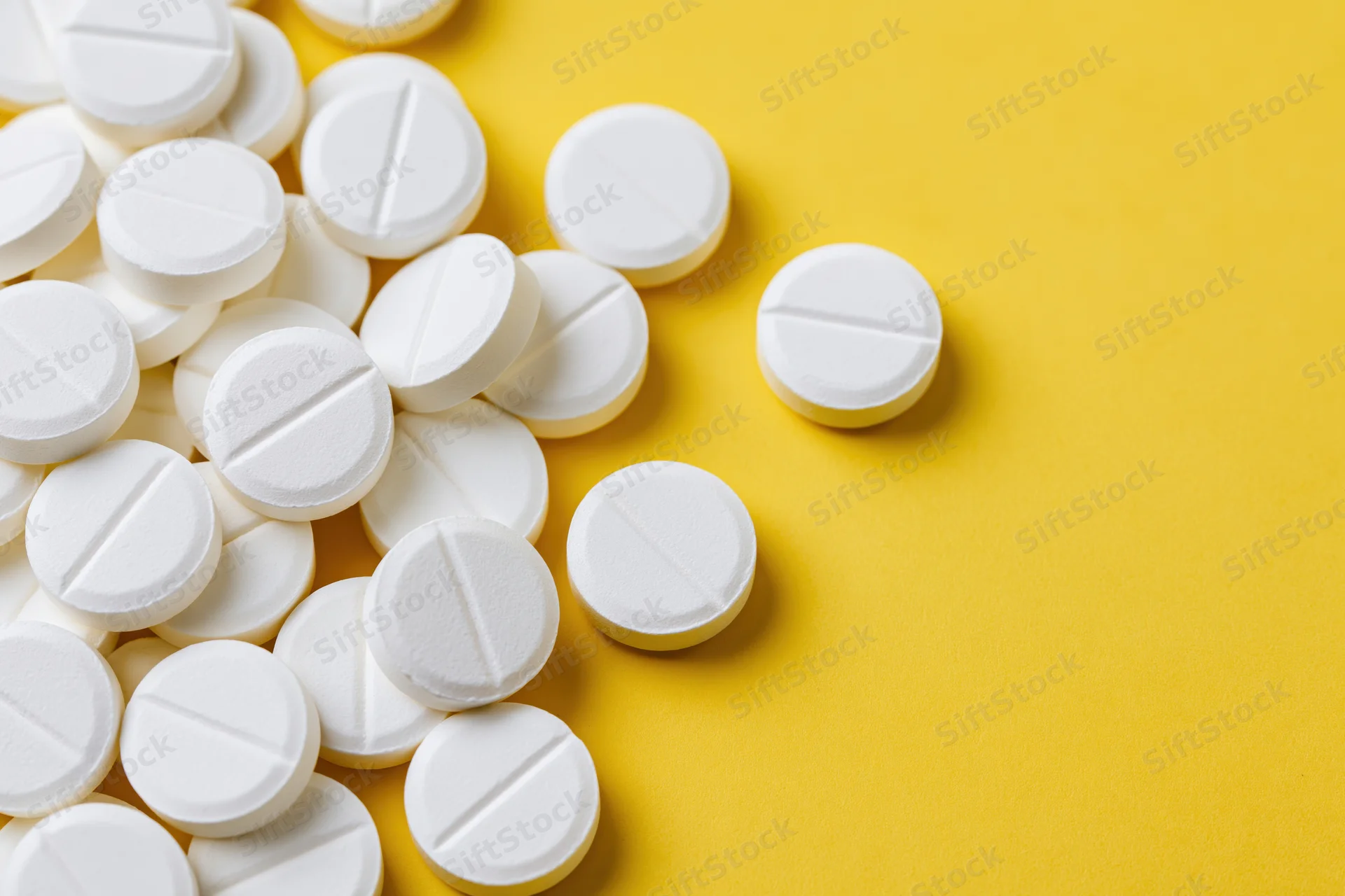 White pharmaceutical tablets scattered on a yellow surface with copyspace