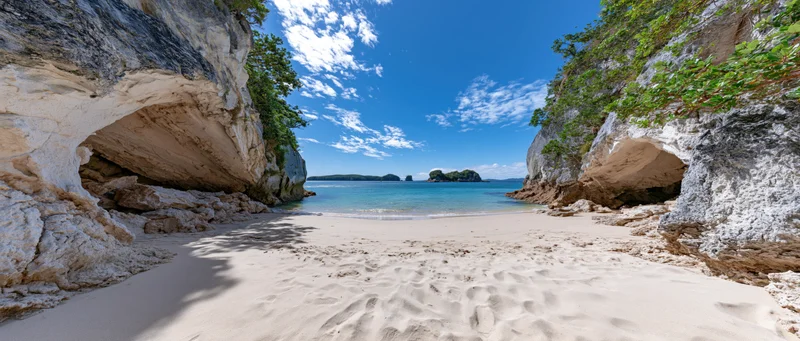Sandy cove framed by eroded limestone cliffs opening to turquoise ocean under blue sky