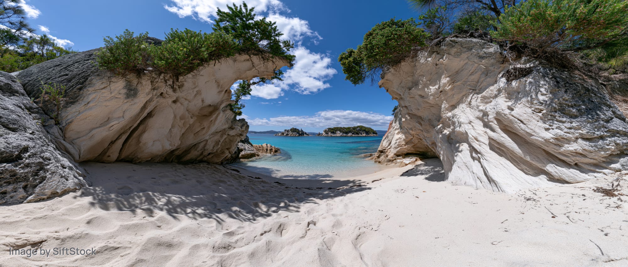 Secluded sandy cove framed by large eroded sandstone rock arch under blue sky with scattered clouds