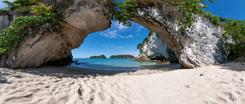 Sandy cove framed by large eroded rock arch overlooking turquoise ocean under blue sky
