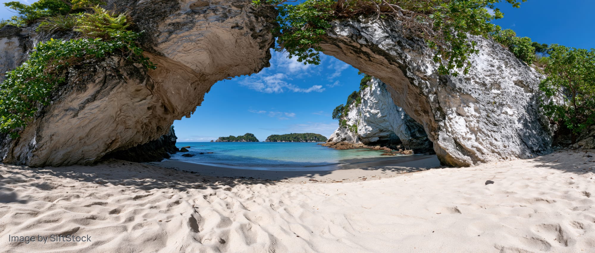 Sandy cove framed by large eroded rock arch overlooking turquoise ocean under blue sky