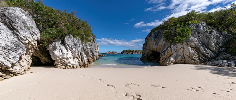 Secluded sandy cove framed by large eroded sandstone rock arches under clear blue sky