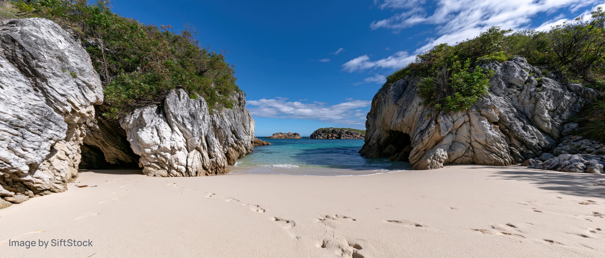 Secluded sandy cove framed by large eroded sandstone rock arches under clear blue sky