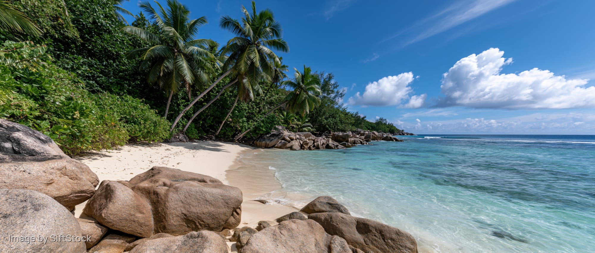Secluded tropical beach with granite boulders along the shoreline under a clear blue sky