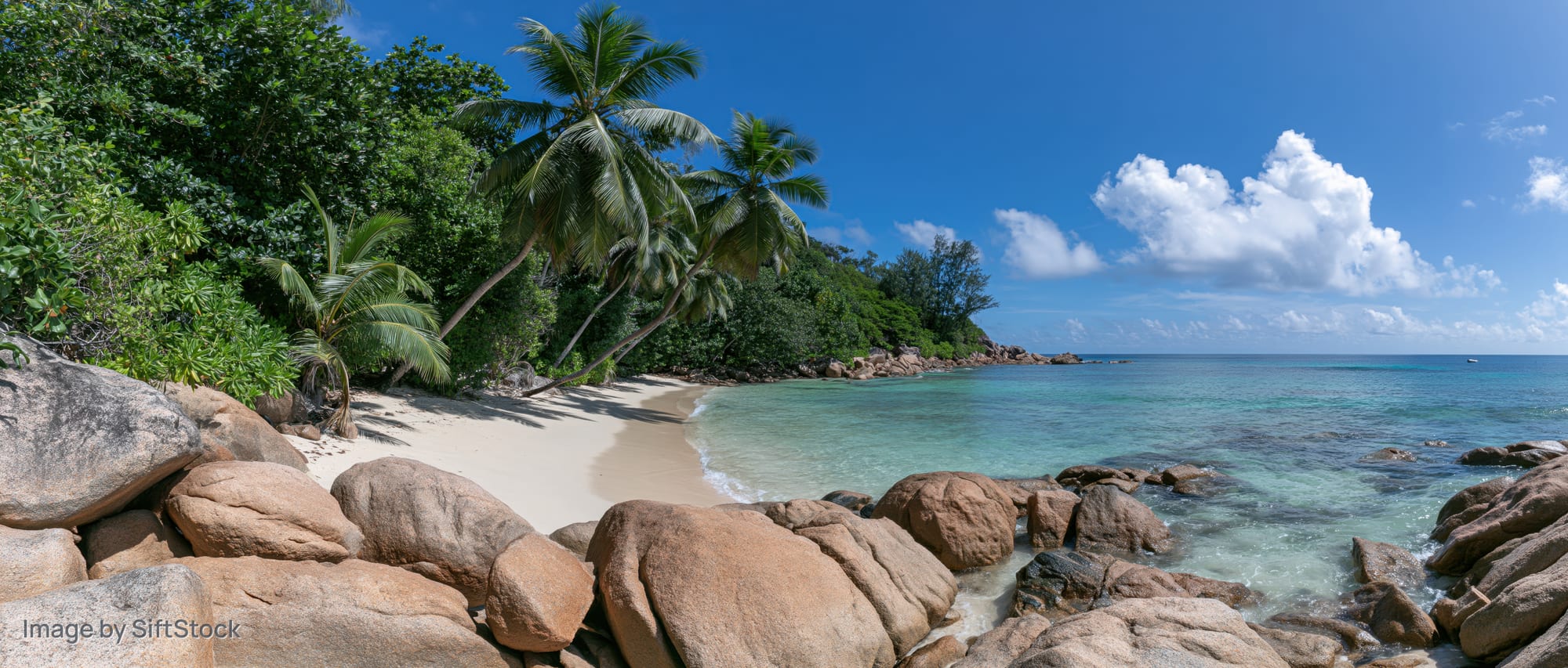 Secluded tropical beach with granite boulders along the shoreline under a blue sky with white clouds