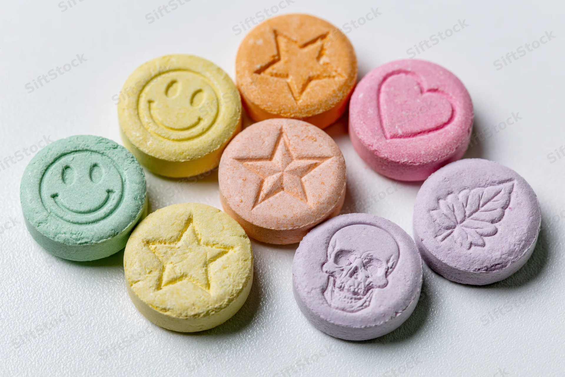 Colorful pressed tablets with smiley, star, heart, skull and leaf designs arranged loosely on white surface