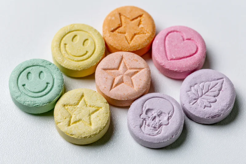 Colorful pressed tablets with smiley, star, heart, skull and leaf designs arranged loosely on white surface