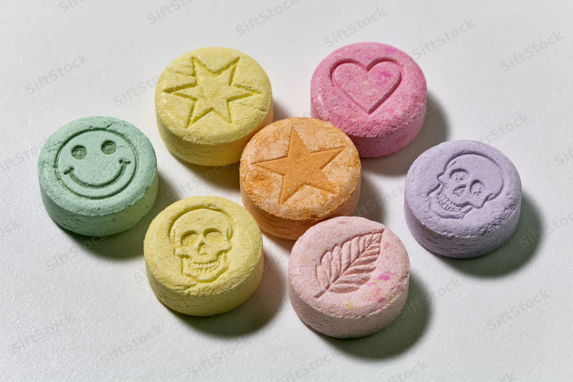 Seven colorful pressed tablets with embossed symbols arranged on a white surface