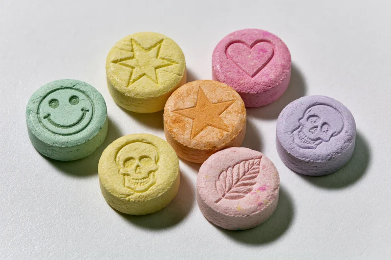 Seven colorful pressed tablets with embossed symbols arranged on a white surface