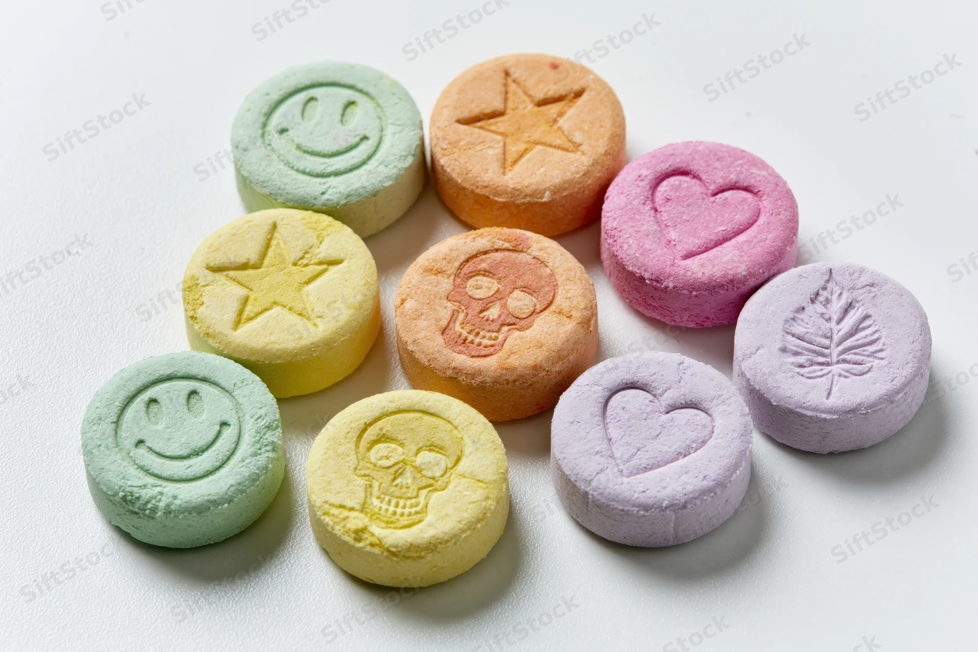 Colorful pressed tablets with smiley, star, heart, skull and leaf designs arranged on white surface