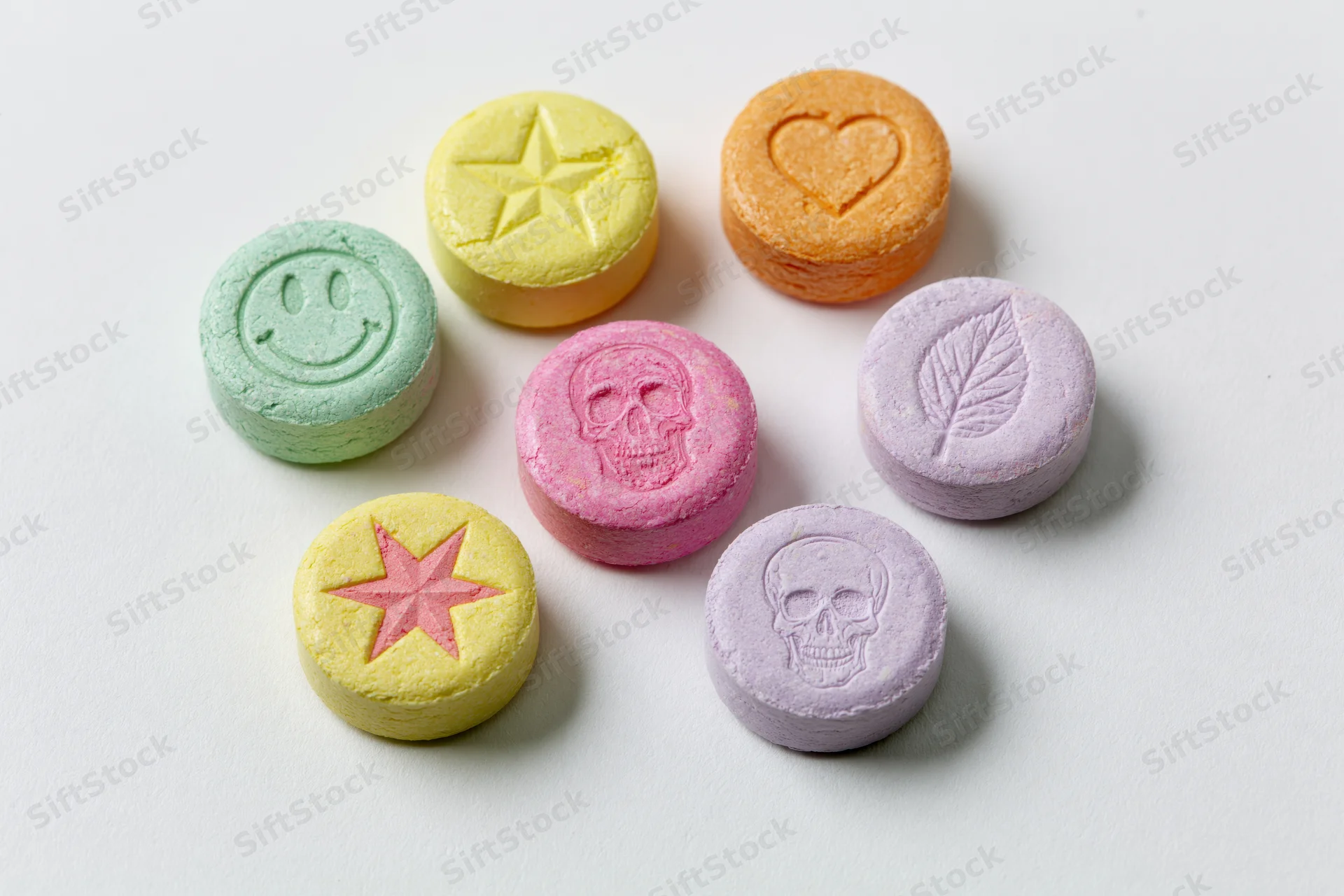 Seven colorful pressed tablets with symbols arranged on white surface