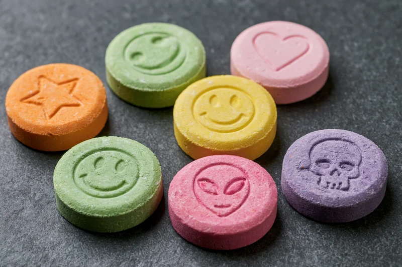 Colorful pressed tablets with smiley, heart, star, alien, and skull imprints on dark textured surface