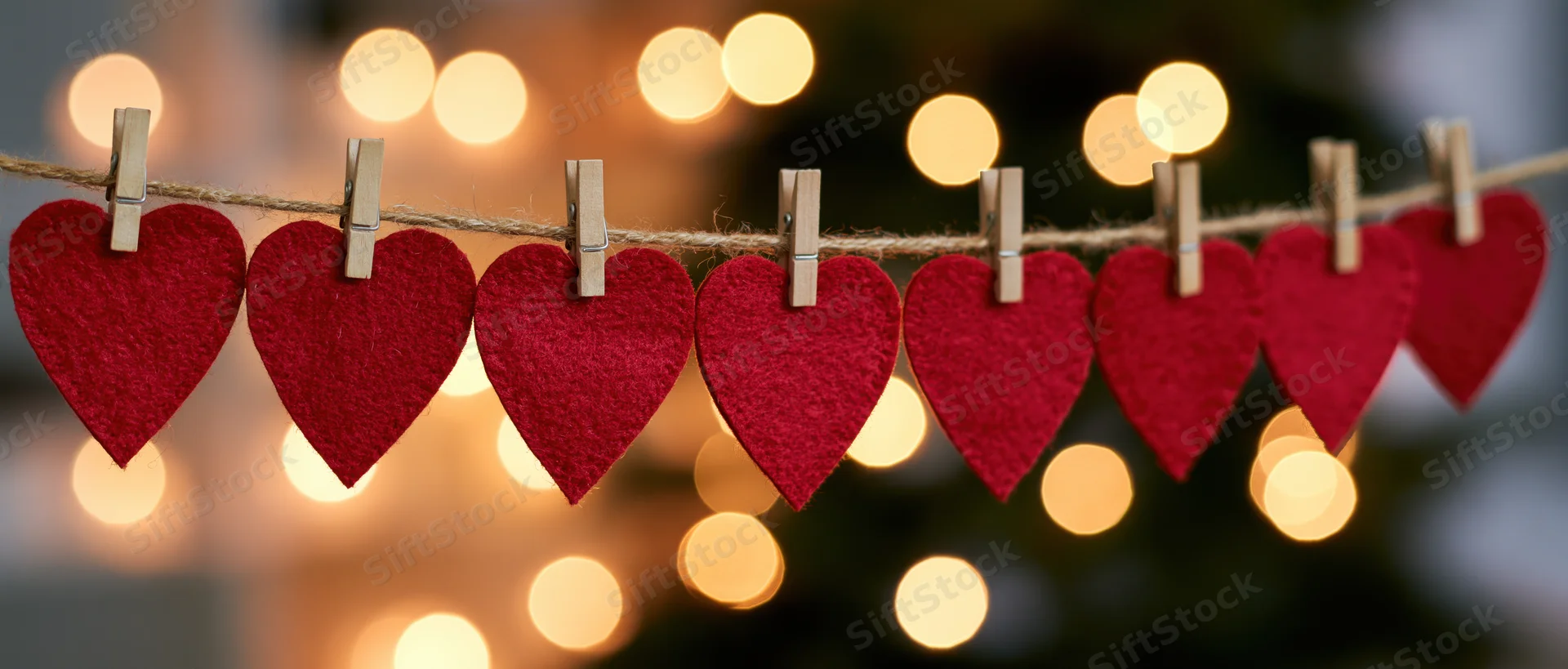 Red felt hearts clipped on a string with wooden clothespins against warm bokeh lights