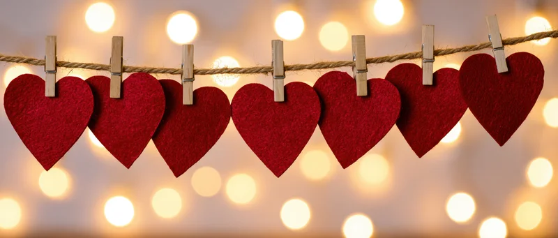 Red felt hearts clipped on a string with wooden clothespins against warm bokeh lights