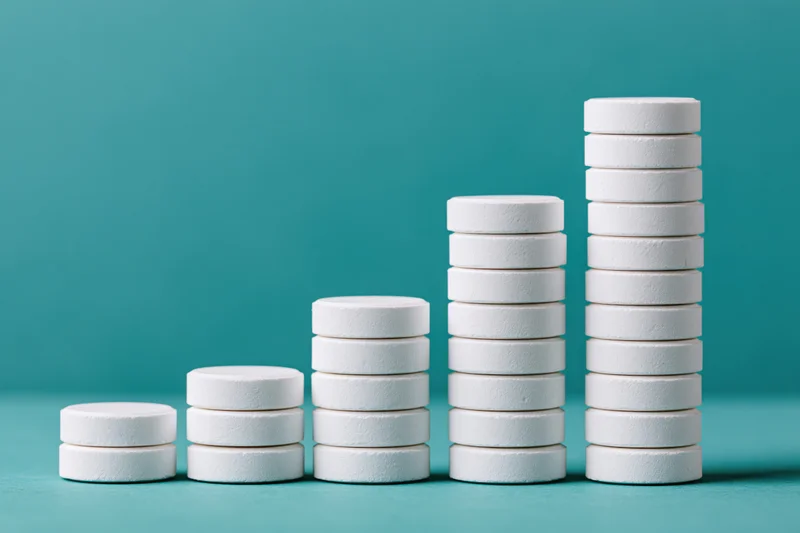 Stacks of white round pharmaceutical tablets arranged in ascending order on a teal surface