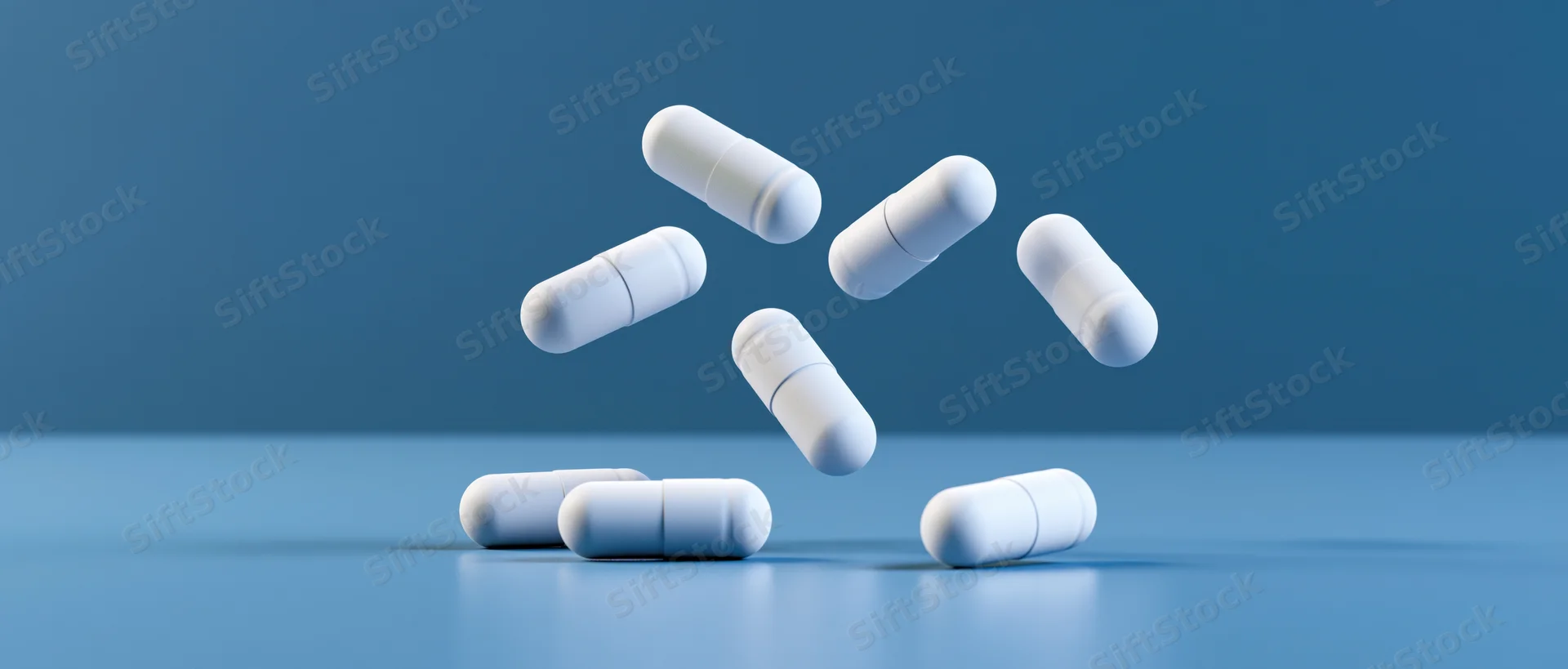 White medical capsules floating and resting on a blue surface