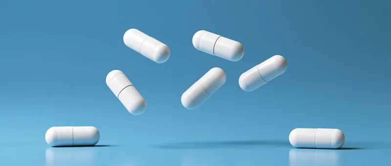 White medical capsules floating midair and resting on a blue reflective surface