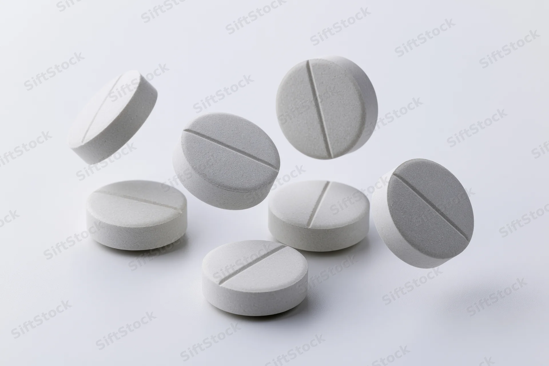 White round pharmaceutical tablets scattered mid-fall against a plain white background