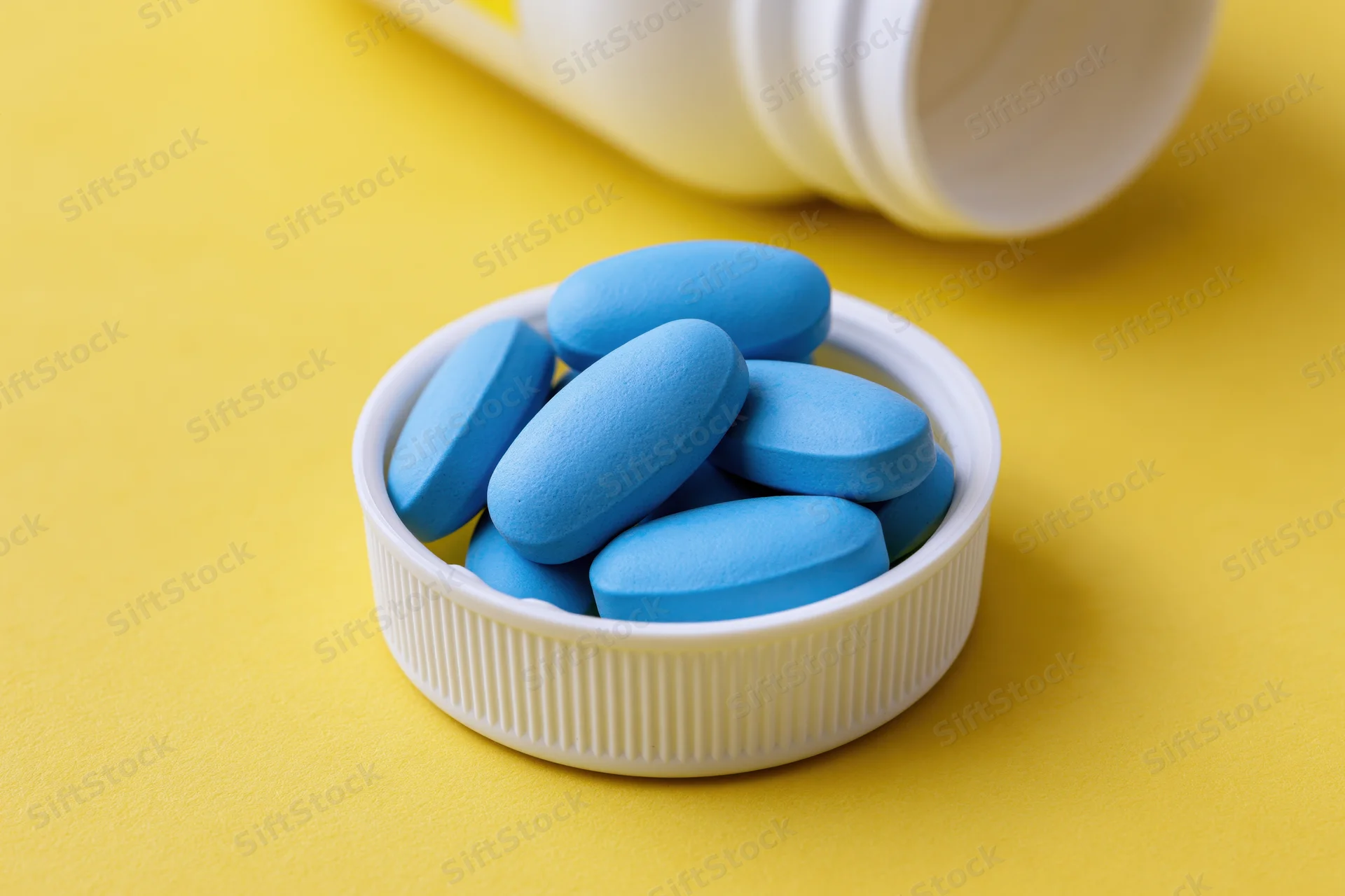 Blue oval pills resting in a white bottle cap on a yellow surface