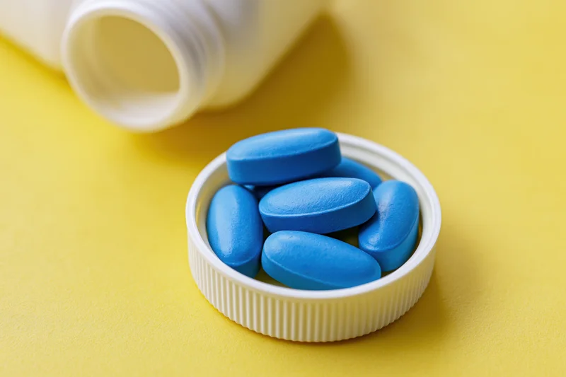 Blue oval pills resting in a white bottle cap on a yellow surface