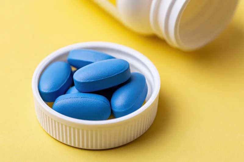 Blue oval pills resting inside a white plastic bottle cap on yellow surface