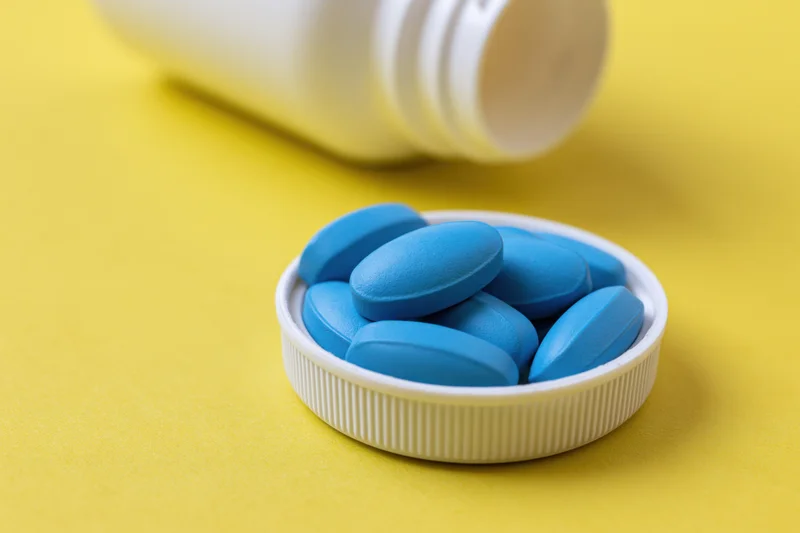 Blue oval pills resting in a white bottle cap on a yellow surface