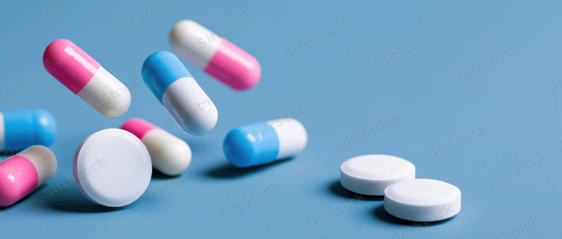 Pharmaceutical capsules and white tablets scattered on a blue surface