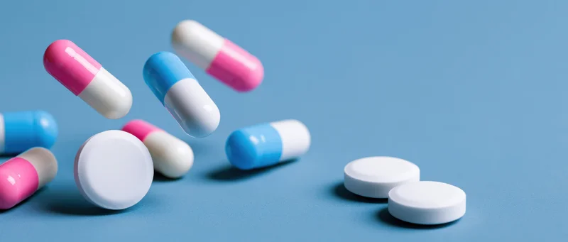 Pharmaceutical capsules and white tablets scattered on a blue surface