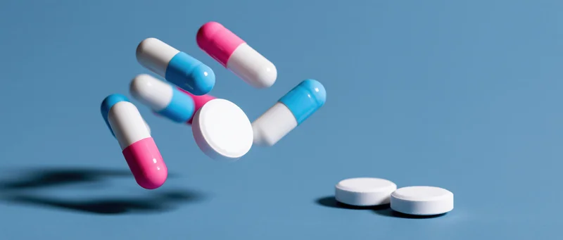 Pharmaceutical capsules and white tablets falling in mid-air against a blue surface