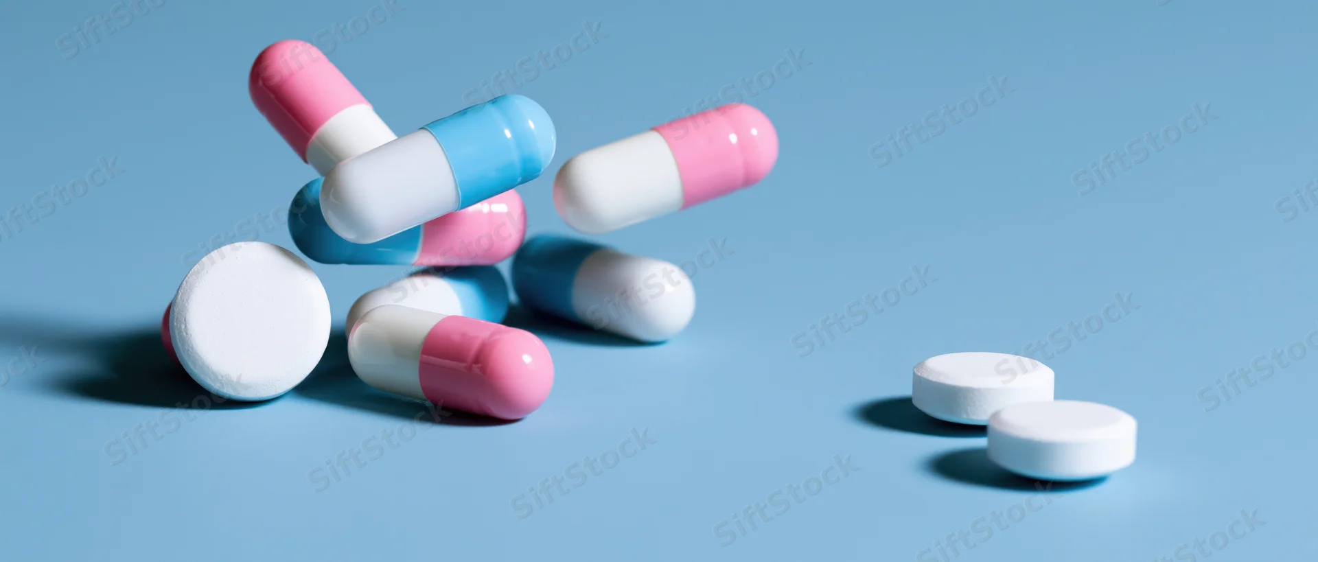 Scattered pharmaceutical capsules and white tablets on a light blue surface