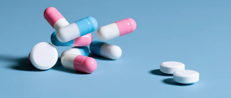 Scattered pharmaceutical capsules and white tablets on a light blue surface