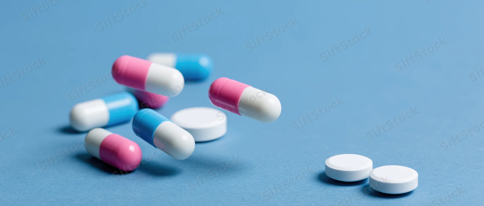 Scattered pharmaceutical capsules and white tablets on a blue surface