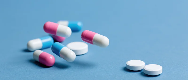 Scattered pharmaceutical capsules and white tablets on a blue surface