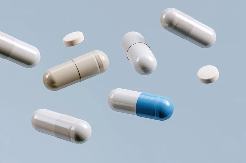 Pharmaceutical capsules and pills floating in midair against a light blue background
