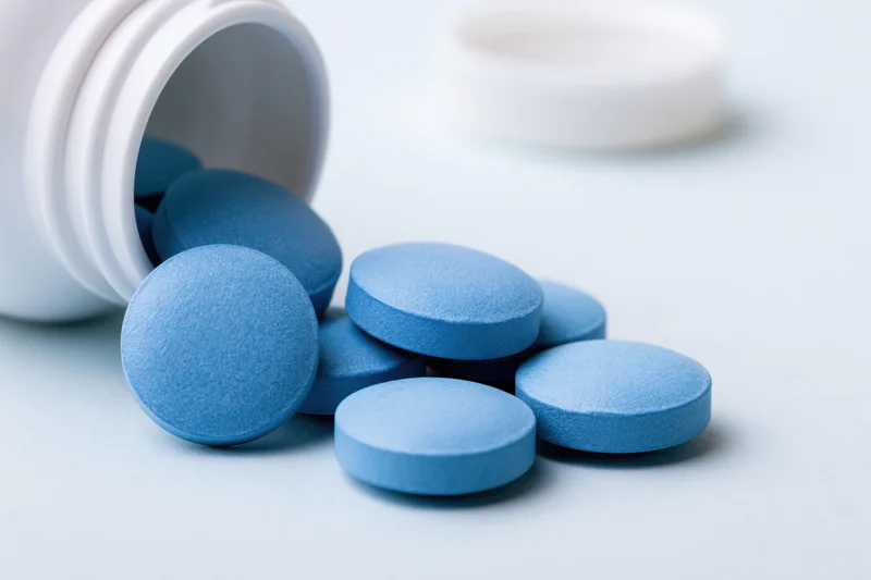 Blue pharmaceutical tablets spilled from a white bottle on a light surface