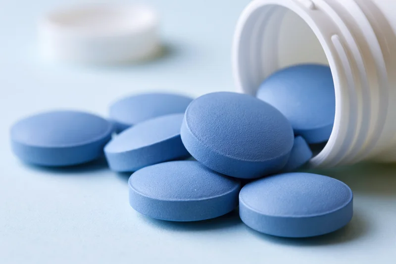 Blue pharmaceutical tablets spilled from a white plastic bottle on a light surface