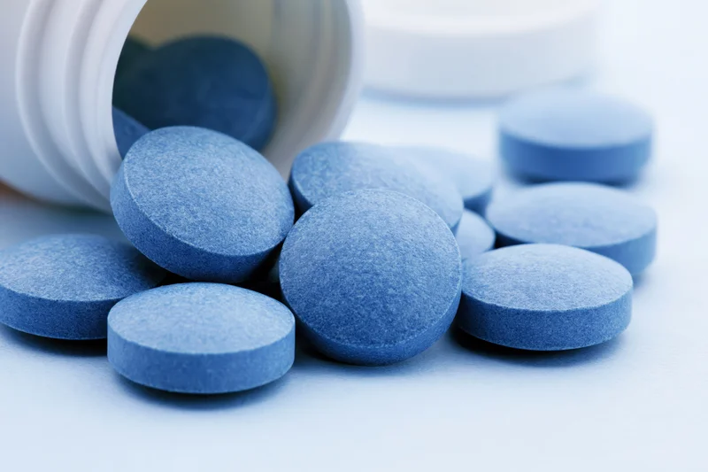 Blue pharmaceutical tablets spilled from a white bottle on a light surface