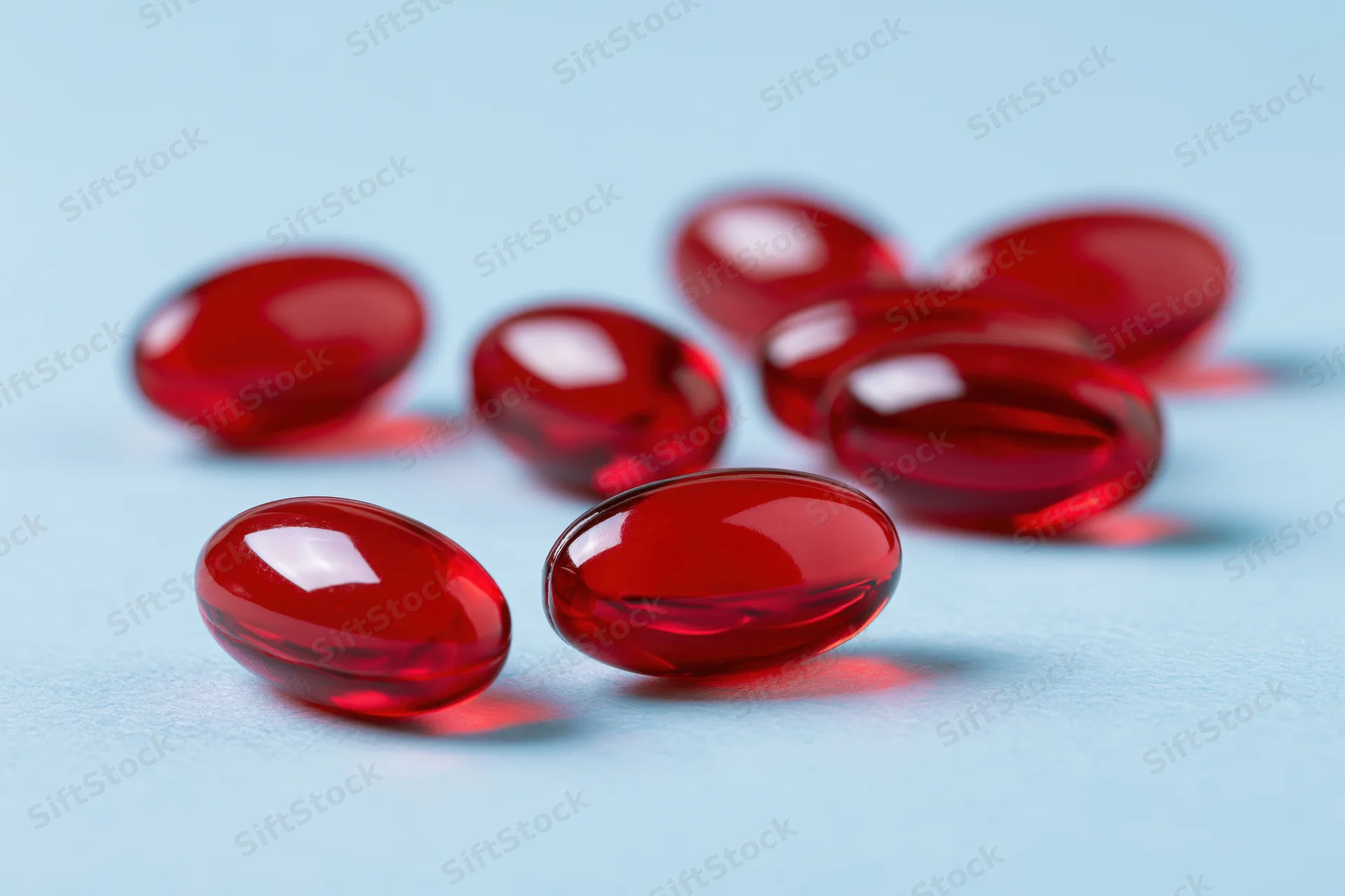 Translucent red gel capsules scattered on a light blue surface