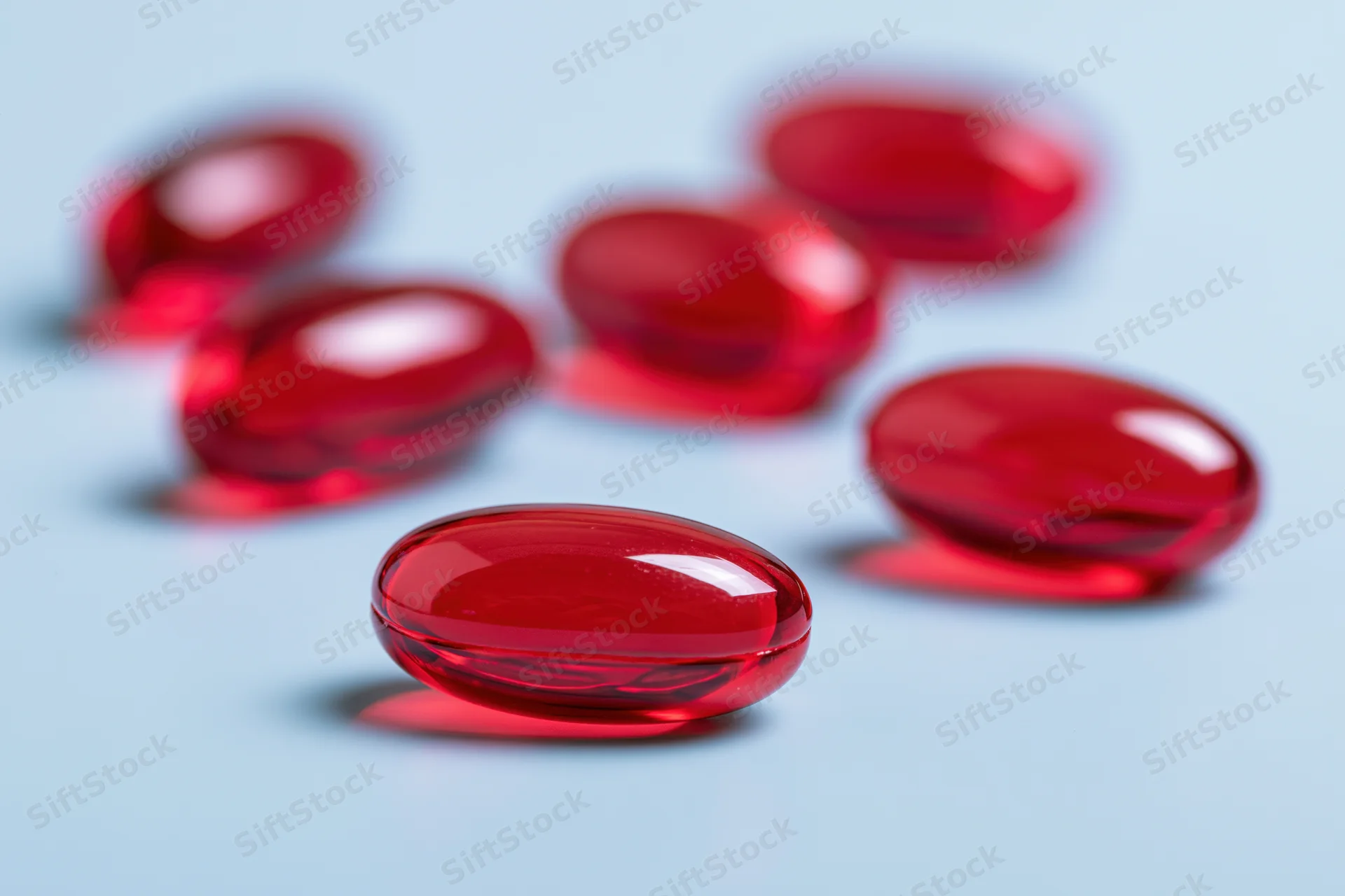Translucent red gel capsules scattered on a light blue surface