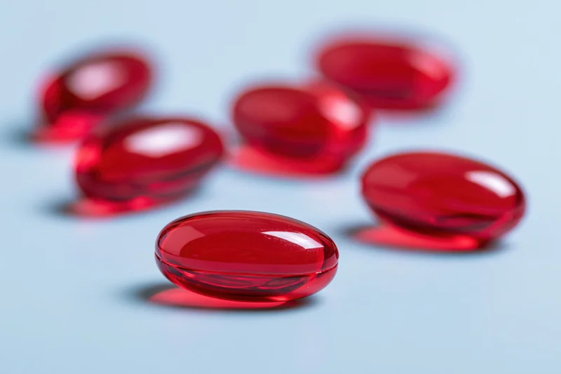 Translucent red gel capsules scattered on a light blue surface