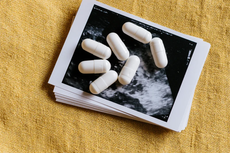White supplement capsules scattered on top of ultrasound images of pregnancy lying on yellow fabric